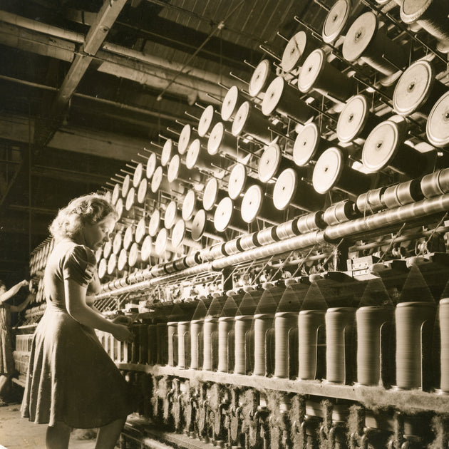 Woman operating vintage textile machinery: Woman working at a large industrial textile spinning machine.